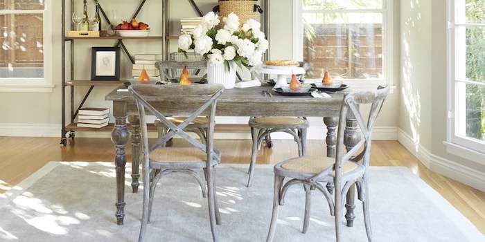 grey-brown antique-looking dining table, with four matching chairs, grey rug and wooden laminate floor, shabby sheek iron shelves, with various items