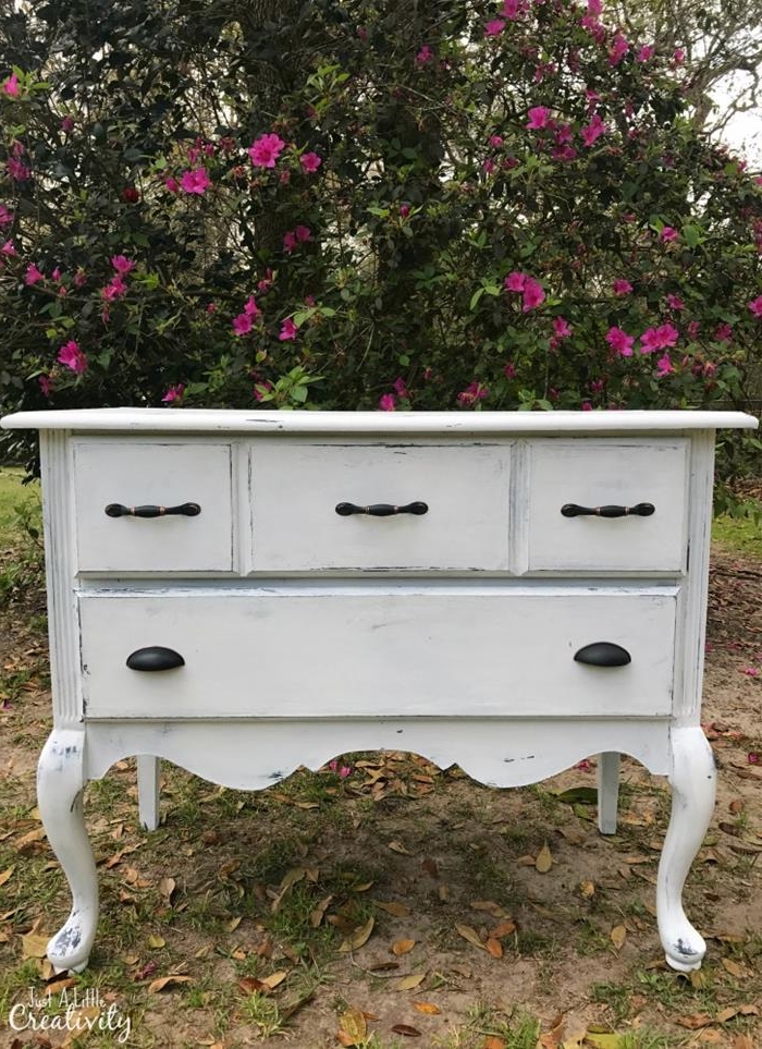 off-white decorative chest of drawers, with black handles, in french antique style, country cottage furniture, placed outside near a blossoming tree