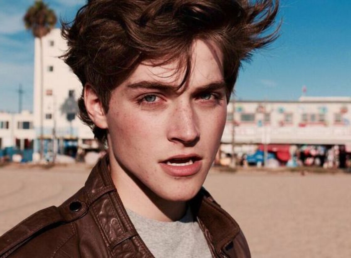 windswept and messy brunette hair, with rebellious look, hairstyles for teenagers, on froy guttierres, in brown leather jacket and pale grey t-shirt