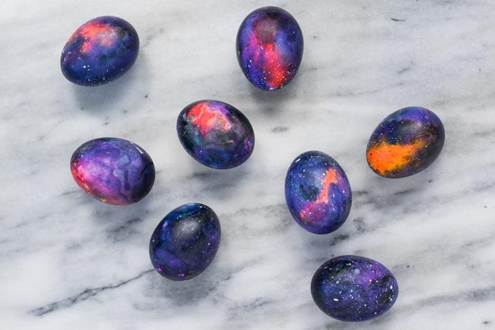 deep space painted in black, navy blue and violet, purple and pink, red and orange, with white dots like stars, on seven hen's eggs, how to dye easter eggs, placed on a marble surface