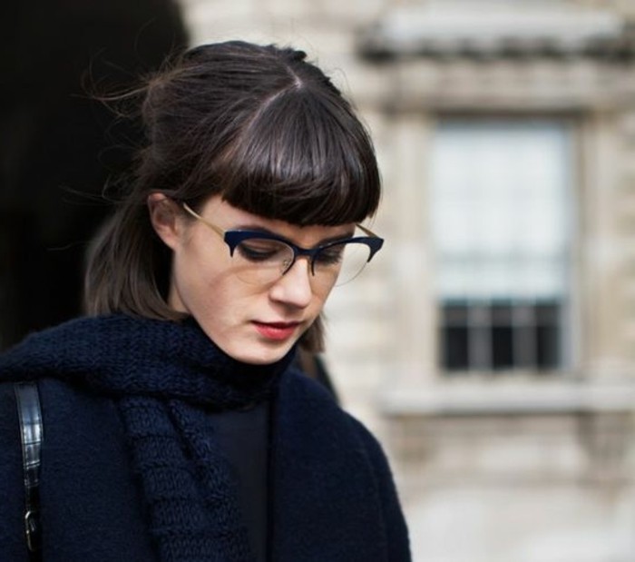 partially tied back hair, with cropped bangs, brunette hairstyles, worn by girl dressed in dark blue, with glasses and chunky knit scarf