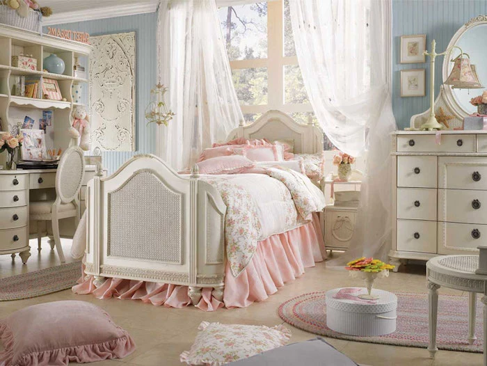 bedroom with pale blue walls, white antique furniture, and matching bed, covered with pale pink and floral bedding, shabby chic decorating, various cushions strewn about