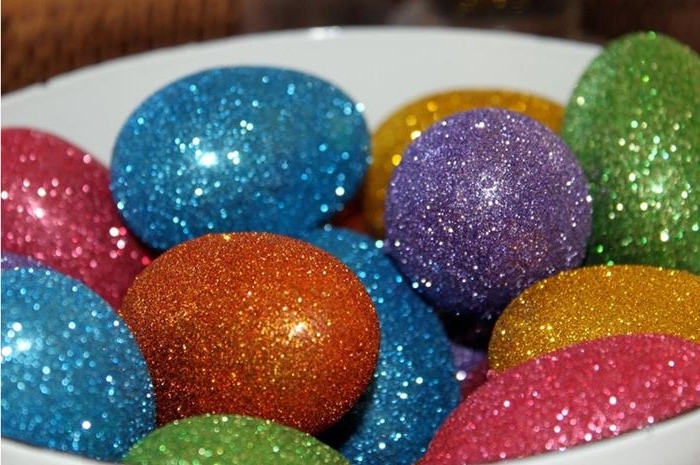 many sparkly glitter covered eggs, in green and orange, yellow and blue, pink and purple, easter egg designs, inside a white dish