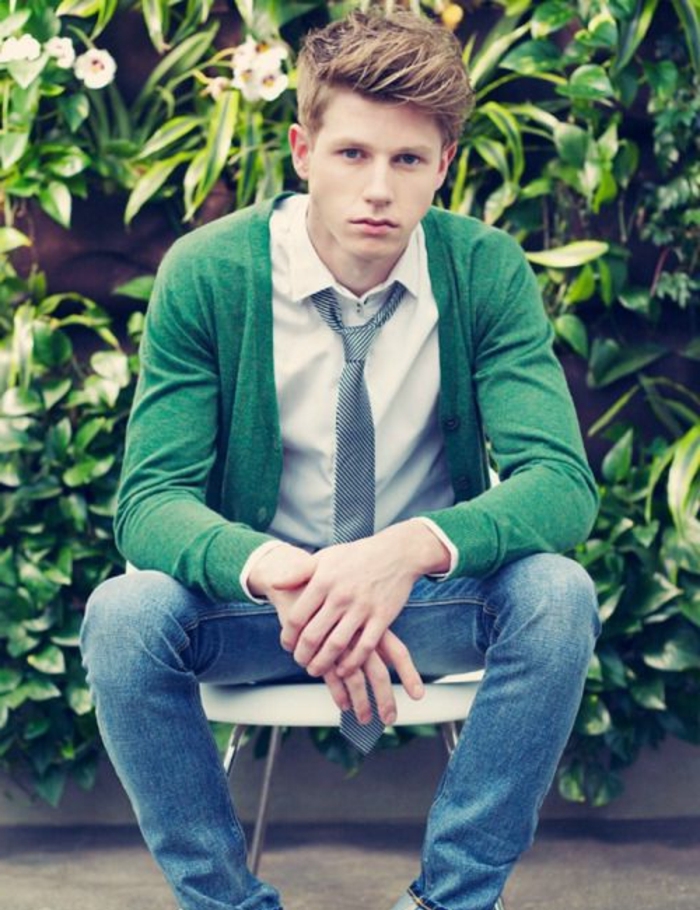 sitting teenager in jeans and white shirt, with grey necktie and green cardigan, dark blonde hair, styled in a messy quiff, short at the sides like in boys fade haircut