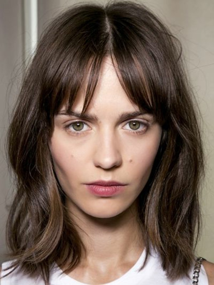 shoulder-length wavy hair, with bangs parted in the middle, brunette hair colors, green-eyed woman, with white sleeveless top, and pale pink lipstick