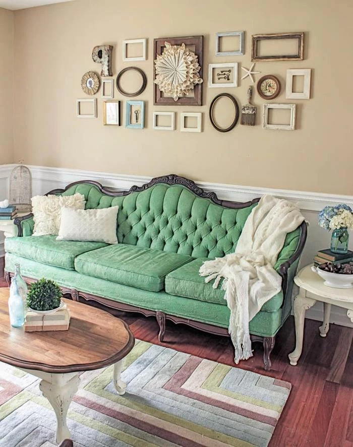 antique green french sofa, with wooden legs and details, two white cushions and a white throw, vintage wooden coffee table, with legs painted white, lots of empty frames on the wall