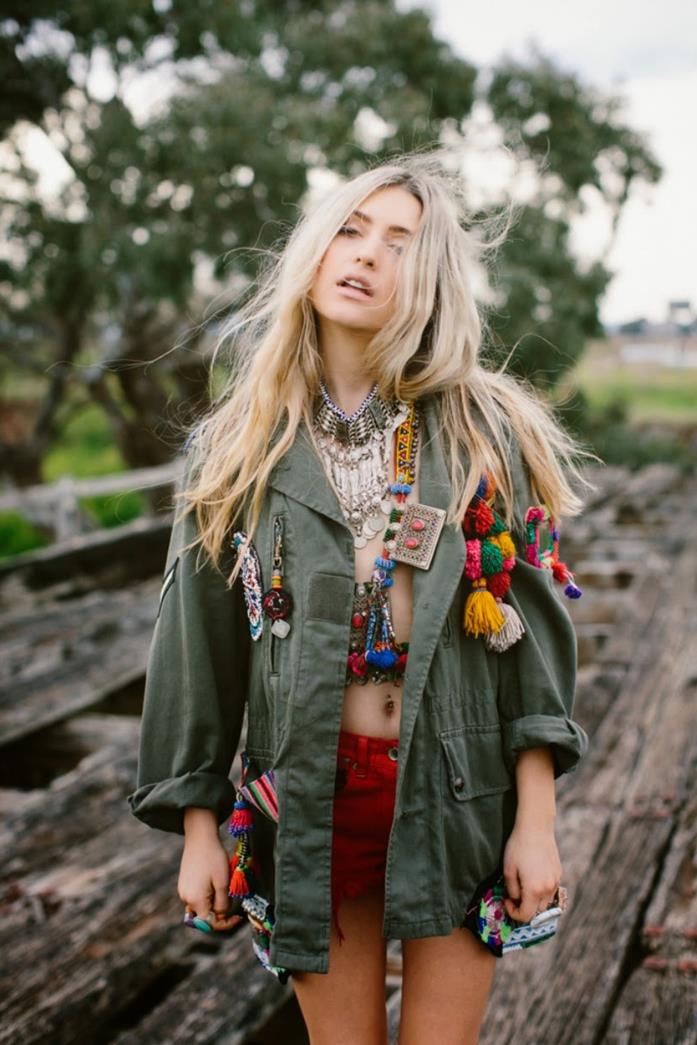 military jacket in green, decorated with boho style aplique details, and colorful pom poms, worn by blonde woman, with long hair, with red shorts, and lots of jewelry