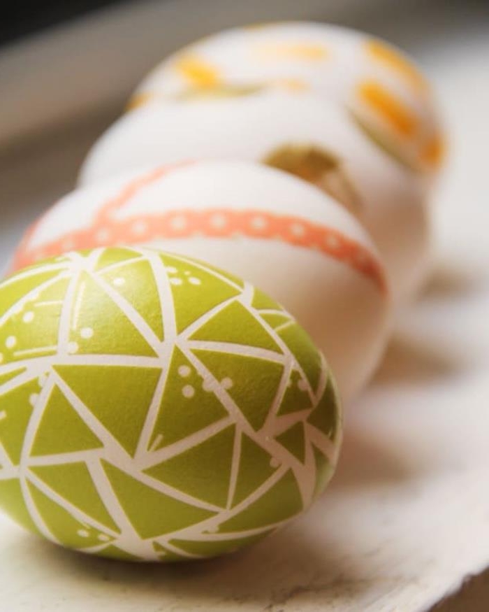 washi tape used as easter egg decoration, on four white eggs, green triangular shapes, orange stripes, brown and yellow shapes