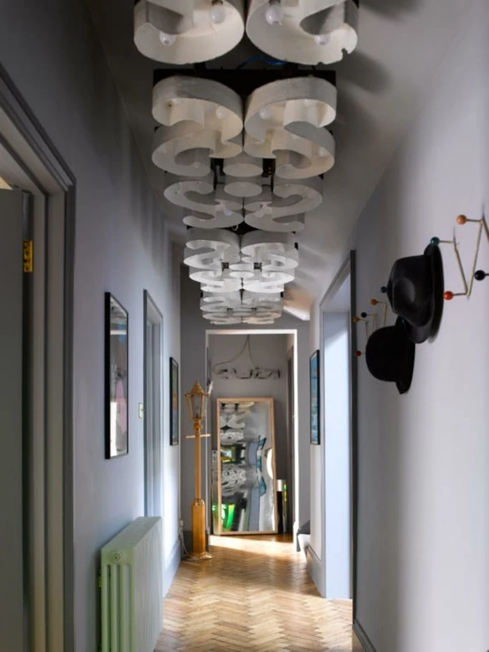 ornate ceiling lights, narrow corridor with pale grey walls, large mirror in wooden frame, hallway decor, laminate floor and coat rack, with two black hats
