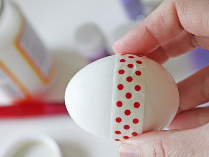 washi tape in white, with red polka dots, stuck around a white egg, held by a hand, coloring easter eggs