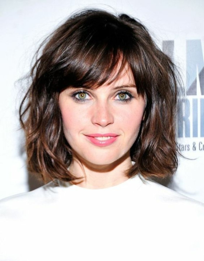 shaggy wavy bob, with side-pated bangs, on smiling woman, with hazel eyes and pale pink lipstick, medium brown hair color, wearing white top