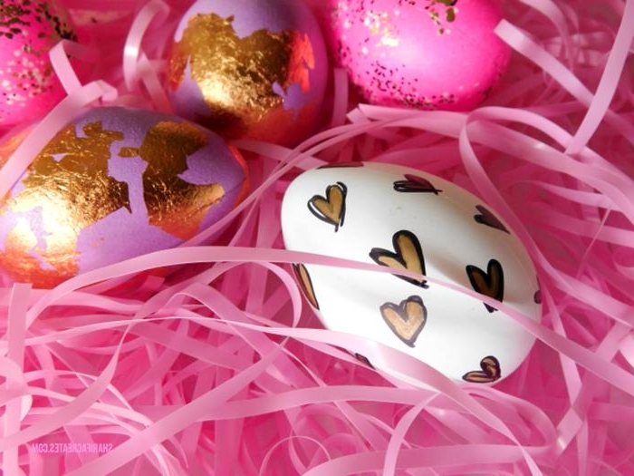 plastic easter grass in pink, two pink eggs, partially covered in gold leaf, one white egg, decorated with hand-drawn hearts, in black and gold