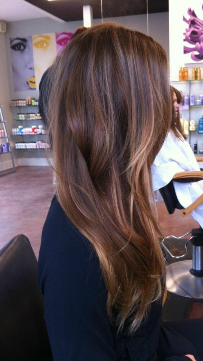 soft layered and wavy, long brown highlighted hair, with natural looking blonde strands, worn by woman in black sweater, sitting on hairdresser's chair