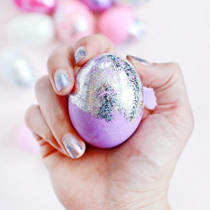 pale purple egg, partially covered with iridescent, hologram-like paint, easter egg designs, held by a hand with matching nail polish