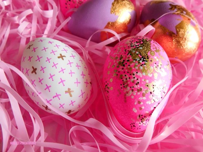 hot pink easter eggs, decorated with white, black and golden dots, or gold leaf, and one white egg, decorated with pink and gold crosses, pink easter grass