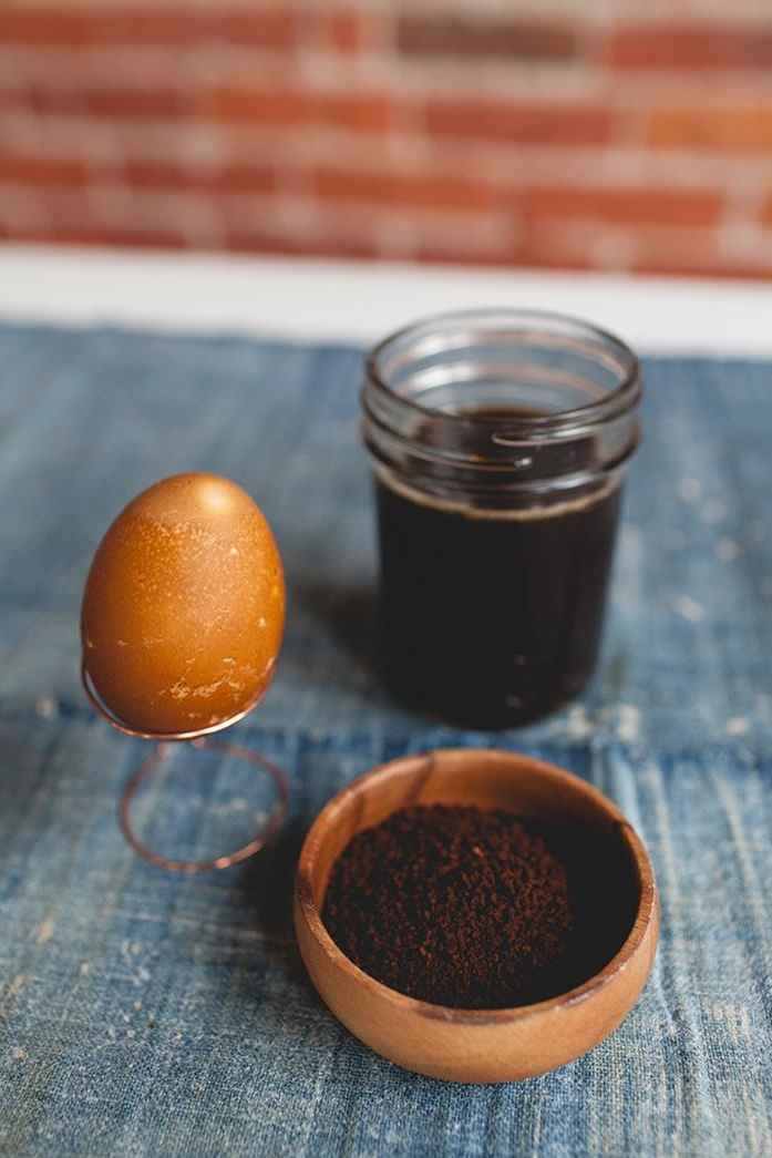 ground coffee in a small clay bowl, near a mason jar filled with dark brown dye, and a beige speckled egg