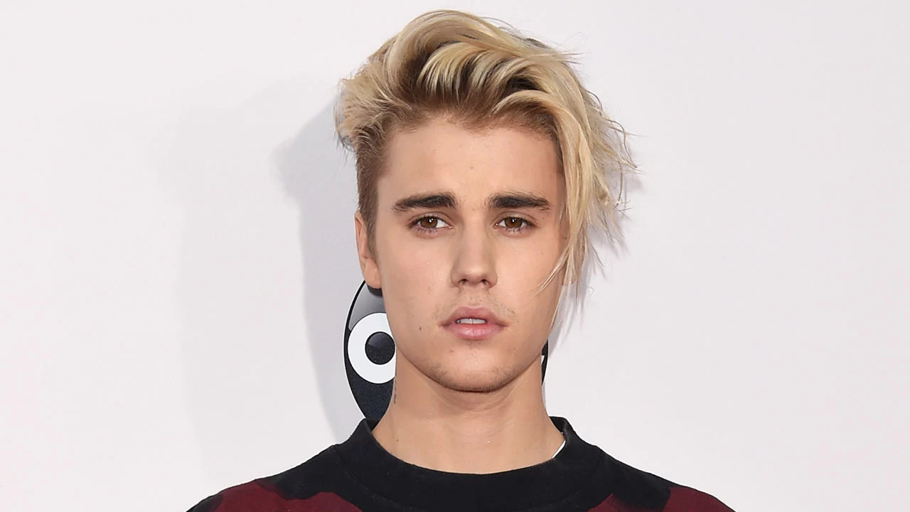 older justin bieber, with chin-length hair, dyed light blonde, with dark roots, bangs swept to one side, long hairstyles for boys