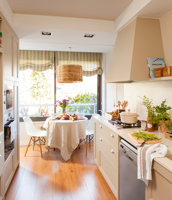 bright kitchen with diningroom space, wooden floors and white walls, cream-colored furniture and appliances, shabby sheek curtains and potted plants