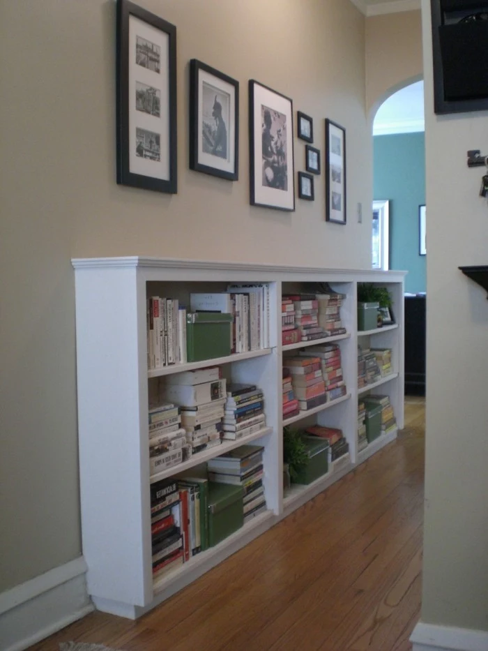 large white cupboard, with shelves containing books and boxes, several photographs in differently sized and colored frames hanging above it, hallway decorating ideas, wooden laminate floor