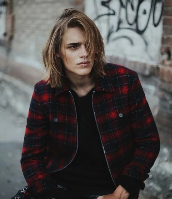 grunge style shoulder-length hair, blonde and layered, long hairstyles for boys, worn by teenager in black jumper, and red plaid jacket