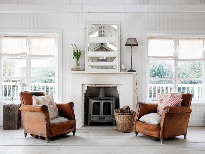 worn leather armchairs, in warm brown, with shabby-chic cushions, off-white wooden floor, fireplace and mirror