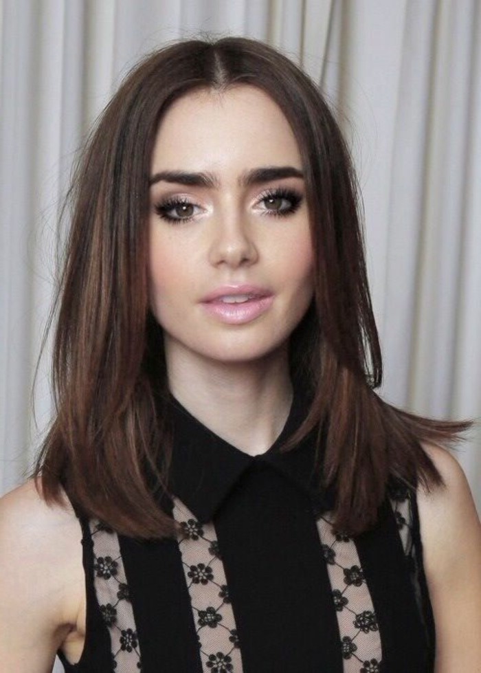 dark haired actresses, lily collins wearing a sleeveless black shirt, with floral lace inserts, brown layered hair, parted in the middle, pale pink lipstick, black mascara and pale purple eye make up