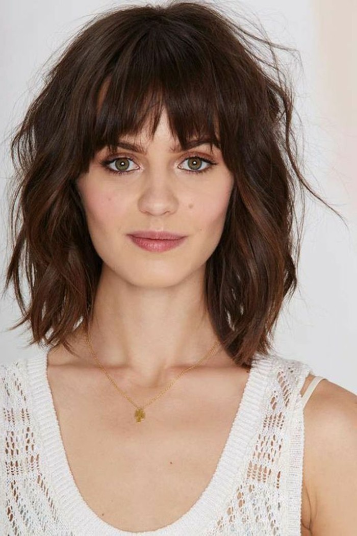 chocolate brown wavy and messy hair, medium brown hair color, and choppy shaggy bangs, on woman with natural looking make up, and green eyes, wearing white meshy tank top