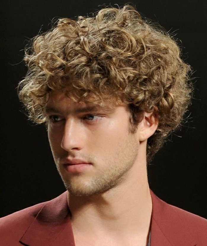 messy dark blonde mop top, naturally curly hair, long hairstyles for boys, on young man with stubble, wearing a red blazer