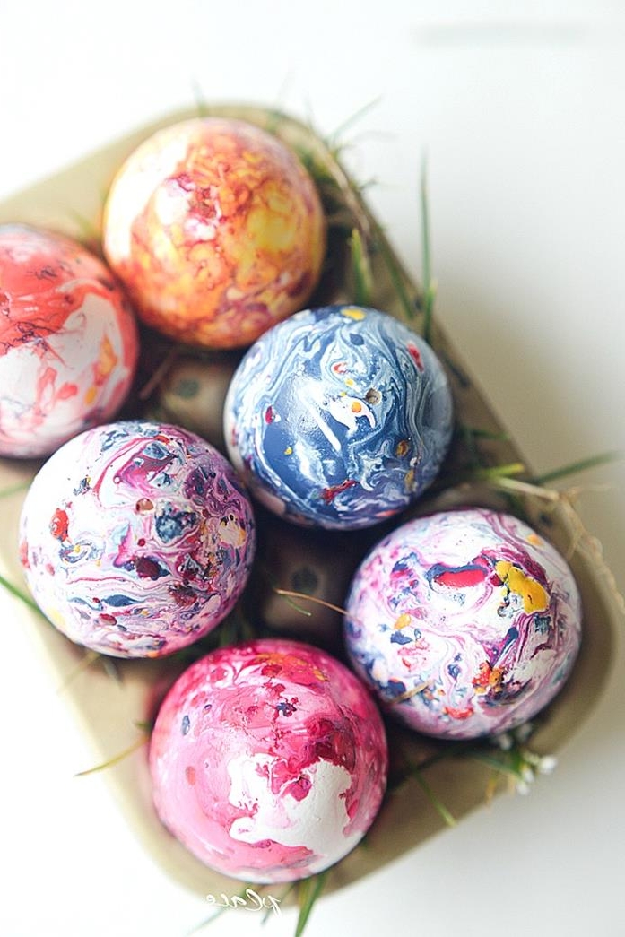 nail polish easter egg coloring, a set of six eggs, dyed in swirly yellow, orange and pink, blue and white, in a cardboard egg box decorated with blades of grass