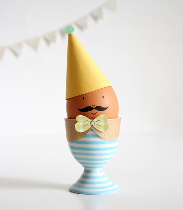 yellow paper party hat, and cardboard collar with bowtie, on egg with minimalistic face and mustache, in a white and blue striped egg dish, easter egg designs
