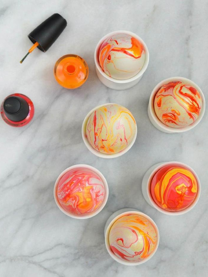 yellow and orange swirly patterns, on easter eggs decorated with nail polish, an open bottle of orange nail polish, and a closed bottle of red nail polish nearby 