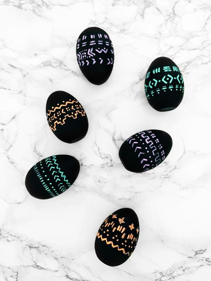 patterns drawn in neon pink, blue and orange, on six black eggs, easter egg ideas, placed on marble surface