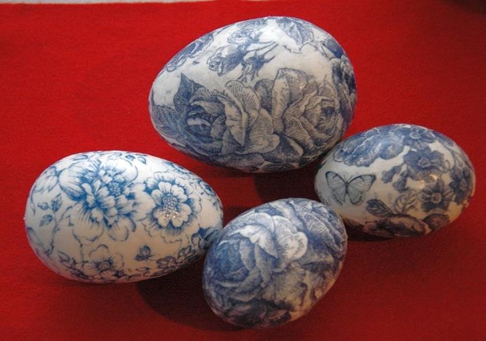 decoupage easter eggs, one large and three smaller, covered in blue floral napkins, with roses and butterflies, intense red background