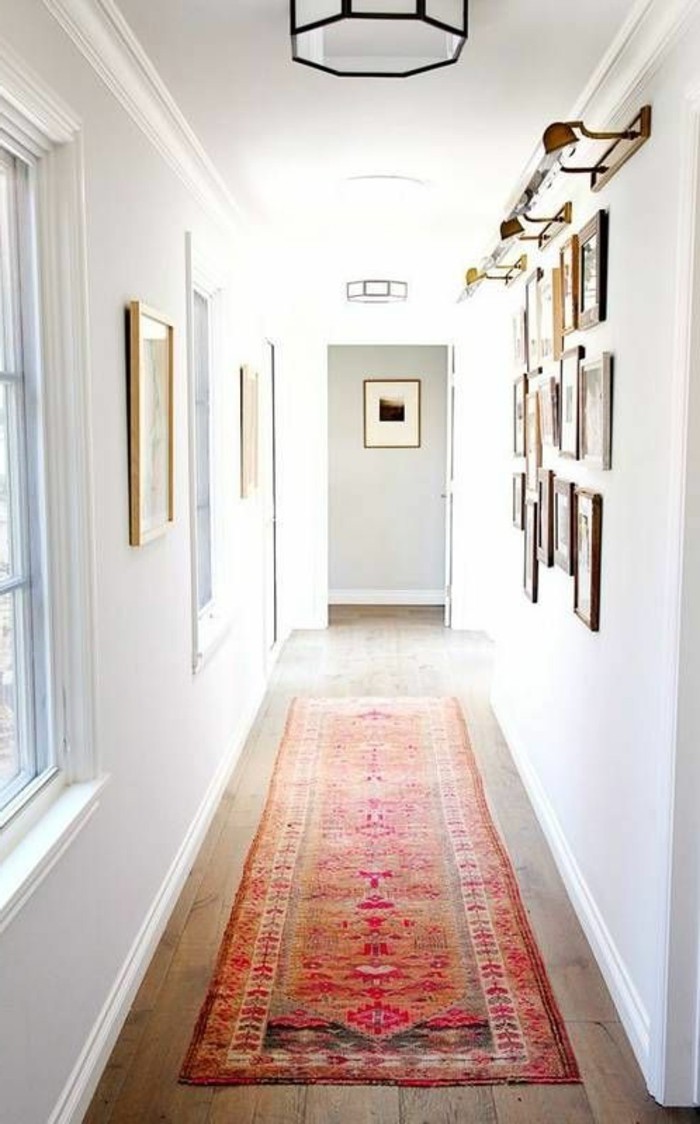 oriental multicolored rug, on wooden floor, inside white corridor, hallway design ideas, with windows and many framed images