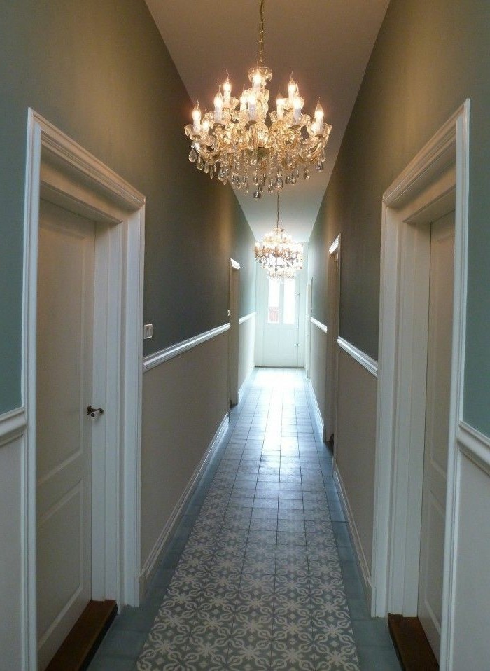 duck's egg blue walls, inside a corridor with white paneling, and four white doors, hallway design ideas, two lit crystal chandeliers, patterned pale blue tiles on floor