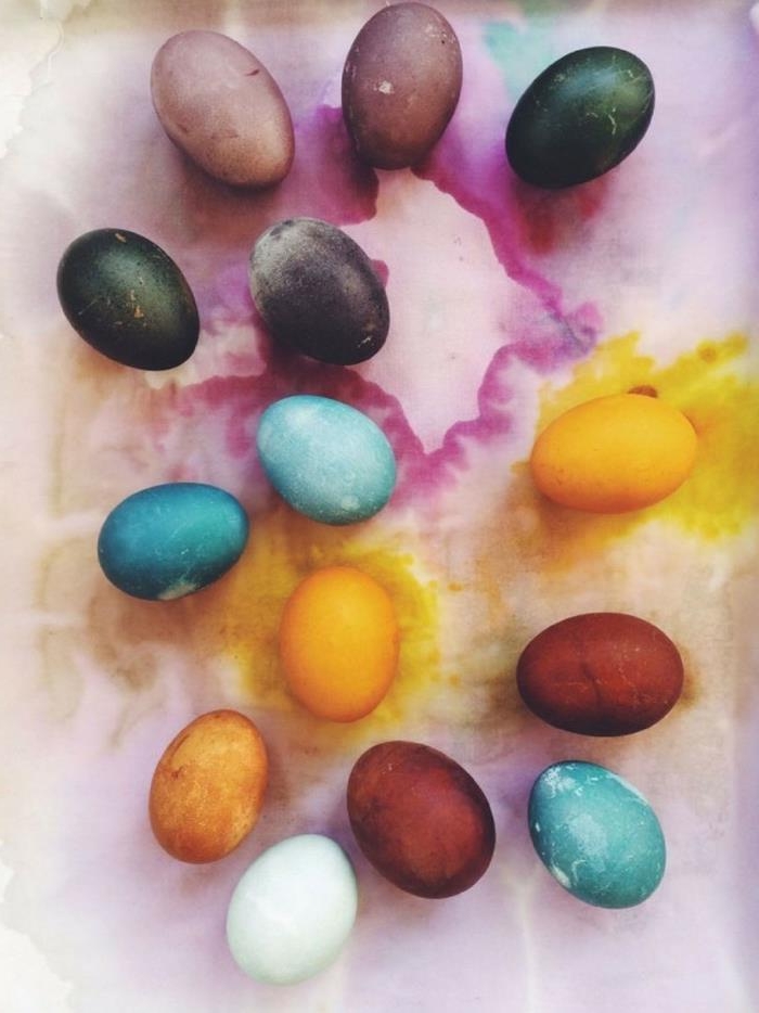 classic easter eggs, dyed with natural colorants, earthy brown and orange, different shades of purple and blue, placed on dye-stained fabric