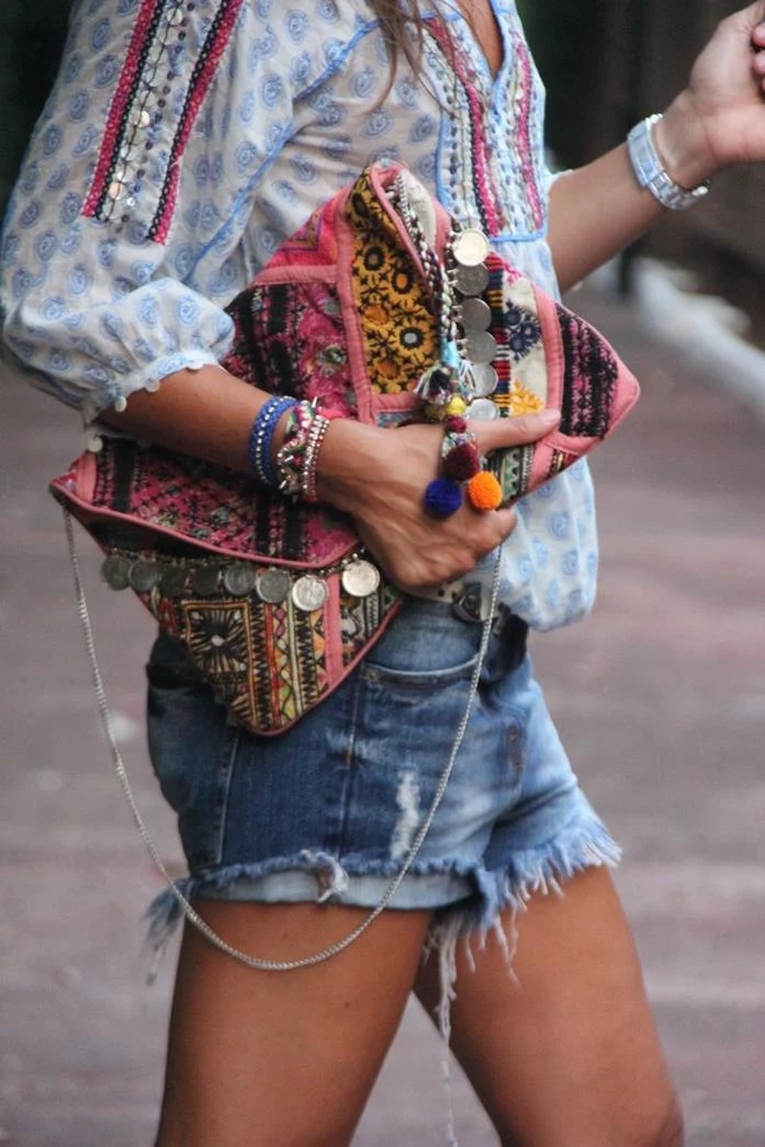 oversized boho fashion clutch, in pink and yellow, with metal beads and thin chainlink handle, held by young woman in shorts and blouse