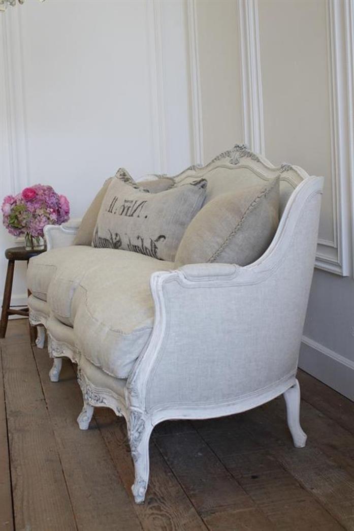 pale grey and white french sofa, with matching cushions, and white armrests and legs, on rough vintage wooden floor, near stool with flower vase