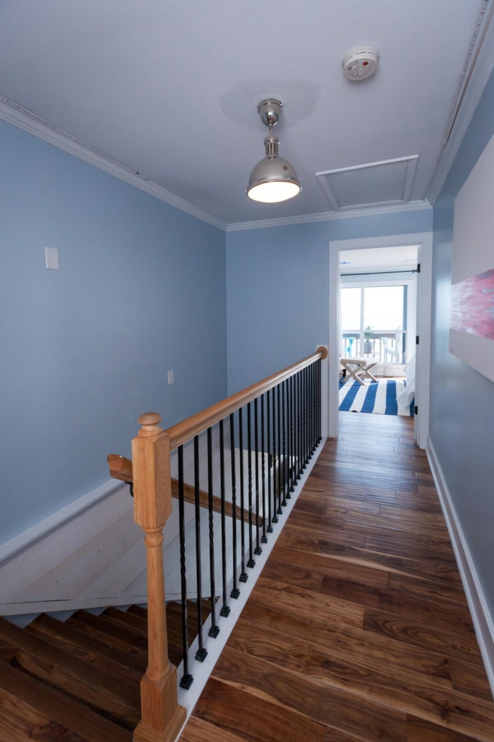 landing with pale pastel blue walls, and white ceiling with a plain light, wooden floors and banisters, hallway decor, framed painting with white and pink