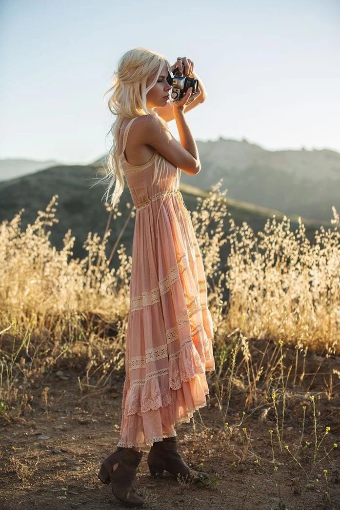 pale pastel pink, tiered sleeveless maxi dress, boho clothing, with frills and lace details, on blonde girl, with brown ankle boots, holding a camera