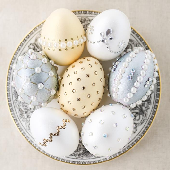 pale peach, silver and white eggs, decorated with stick-on white pearls, silver and gold gem stickers, dying easter eggs, inside a white dish, with grey decorations