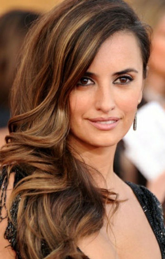 highlighted dark brunette hair, with a deep side parting, and partially curled, worn by penelope cruz, with natural-looking make up, and sparkly black top