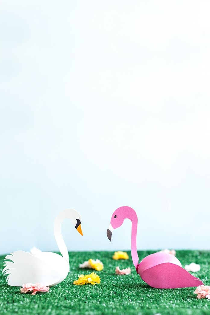 coloring easter eggs, swan and flamingo, made from eggs, one white one dyed pink, with paper wings and heads, placed on artificial green grass, with several tiny fake flowers