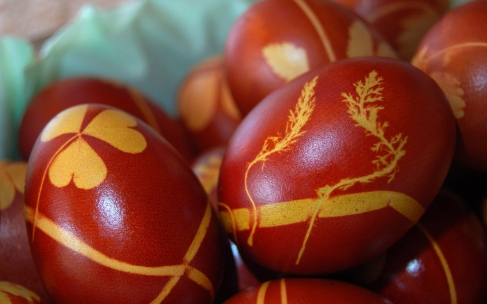 botanical shapes in yellow, printed on red eggs, easter egg coloring the traditional way