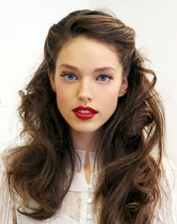 messy and wavy, partially tied back hairstyle, with side-swept, retro-inspired bangs, medium length brown hair, worn by woman in white semi-sheer top, with bright red lipstick, black eyeliner and fake lashes