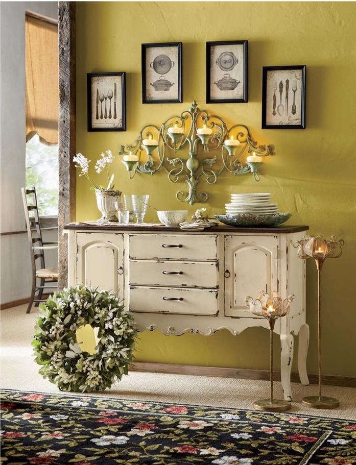 plates and glasses, on large cupboard in cream, with chipped paint effect, near a floral rug in black and green, red and blue, a wreath and several candle holders