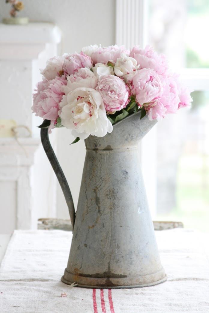 jug made from rusty metal, with curved handle, containing pale pink peonies, country cottage furniture, rough cream tablecloth, with three red stripes
