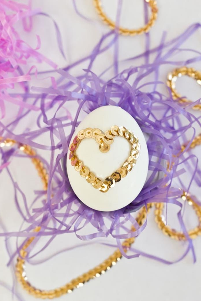 plain white egg, decorated with heart shape, made from golden sequin rope, placed on purple and pink easter grass