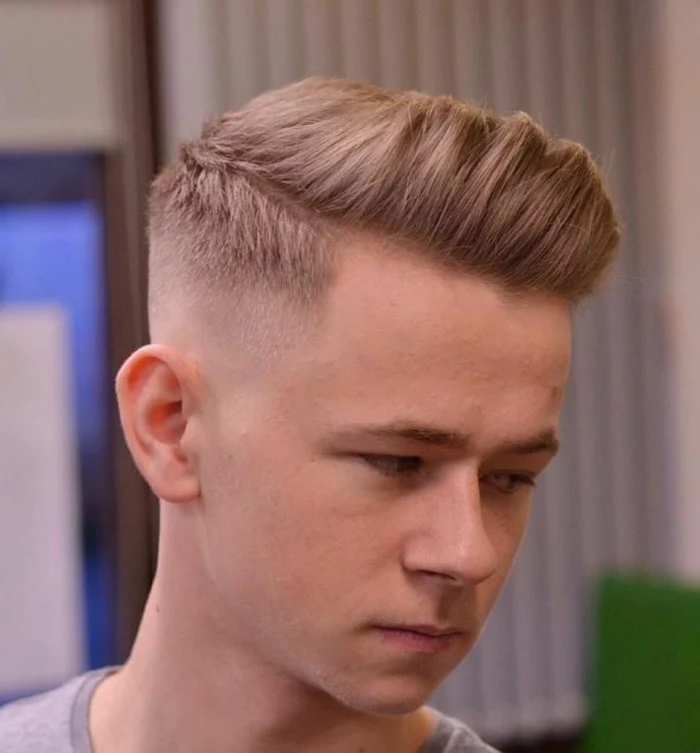 quiff on blonde hair, with a disconnected undercut, boys fade haircut, on young man with serious expression