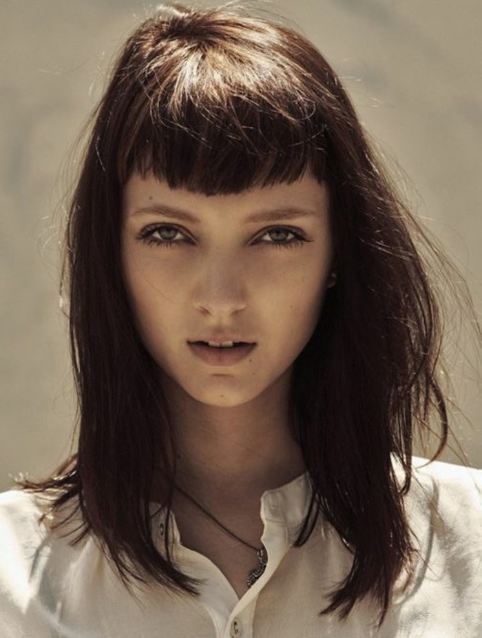 brunette hair colors, wavy shoulder-length haircut, with cropped bangs, worn by blue-eyed young woman, in white shirt